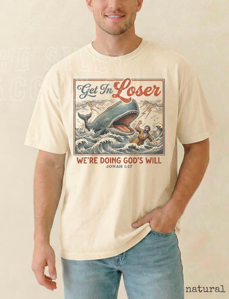 A man wearing a white t-shirt with a graphic design depicting a whale and a person, along with the text "Get In Loser" and "WE'RE DOING GOD'S WILL" printed on it.
