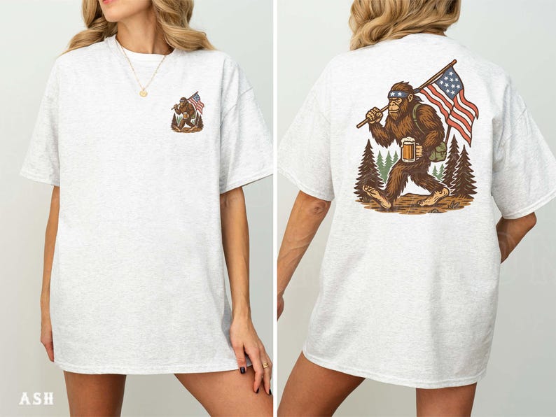 K&ouml;nnte beinhalten: Hellgraues T-Shirt mit einem Bigfoot-Motiv und einer amerikanischen Flagge. Auf der Vorderseite befindet sich ein kleines Bigfoot-Design, w&auml;hrend die R&uuml;ckseite eine gr&ouml;&szlig;ere Illustration von Bigfoot mit einer Flagge und einem Bier zeigt. Das T-Shirt besteht aus einem weichen, bequemen Material.