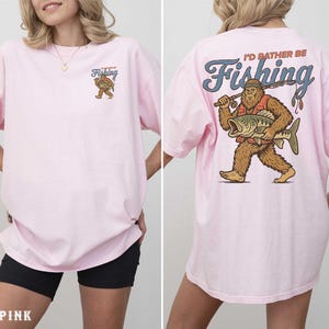 A woman wearing a pink t-shirt with a cartoon image of a giant fish and the text "I'd rather be fishing" printed on the back.