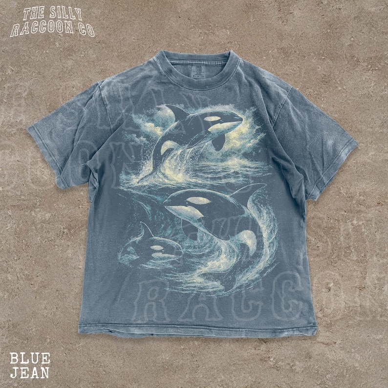 A blue t-shirt with a graphic design of two killer whales in the ocean.