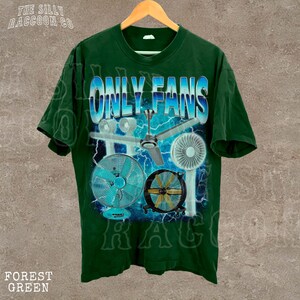 A green t-shirt with a graphic design featuring a fan and various other objects, along with the text "ONLY FANS" prominently displayed.