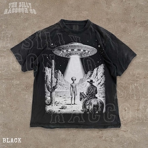 The image is a t-shirt design featuring a scene with an alien spacecraft hovering above a desert landscape, where a man on a horse is present.