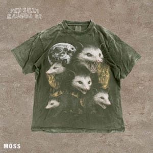 A t-shirt with a graphic design featuring multiple opossum faces with open mouths, arranged in a layered manner.