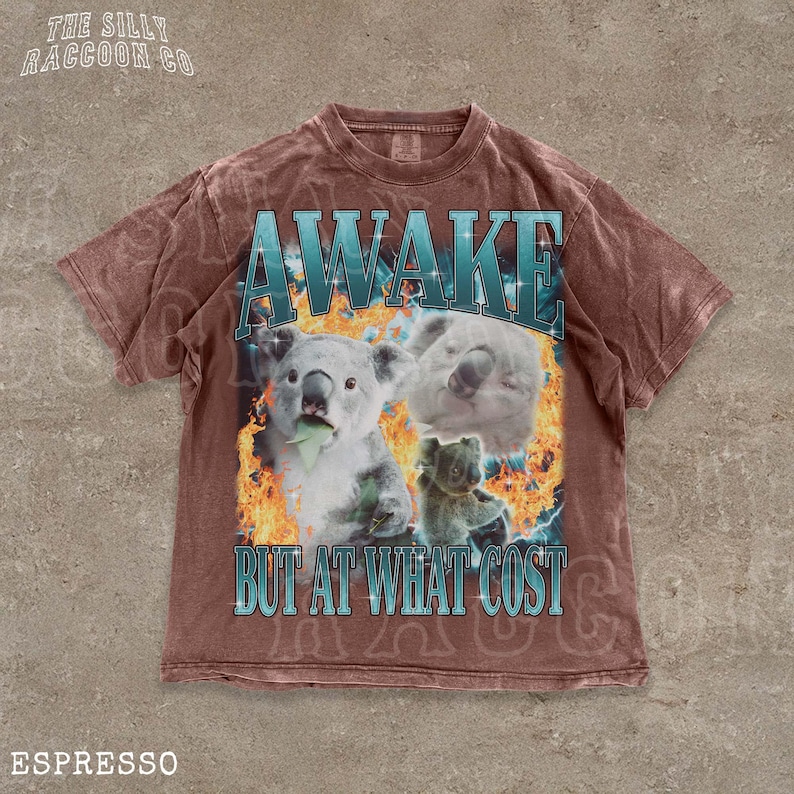 A t-shirt with a graphic design featuring two koalas and the text "AWAKE BUT AT WHAT COST" printed on it.