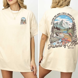 a woman wearing a cream-colored t-shirt with a graphic design on the back. The design includes a fish, mountains, and a Bible verse.