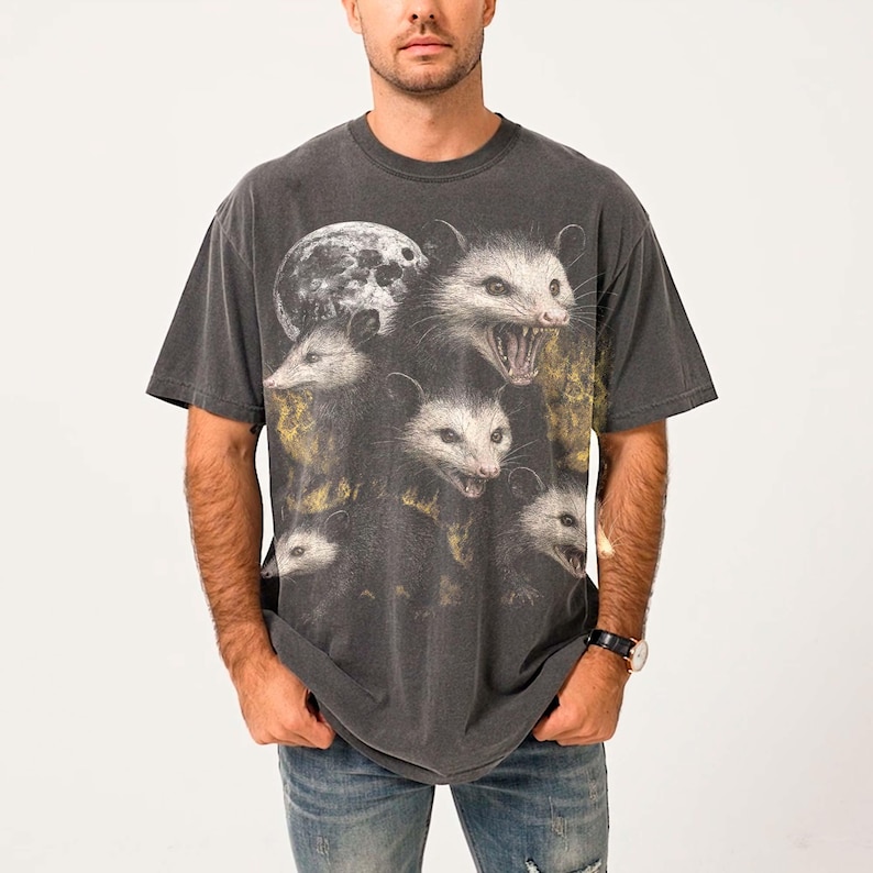 A man wearing a gray t-shirt with a graphic design of multiple opossum faces.