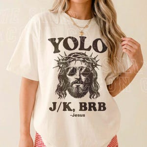 A woman wearing a white t-shirt with a graphic of Jesus and text that says "YOLO J/K, BRB - Jesus".