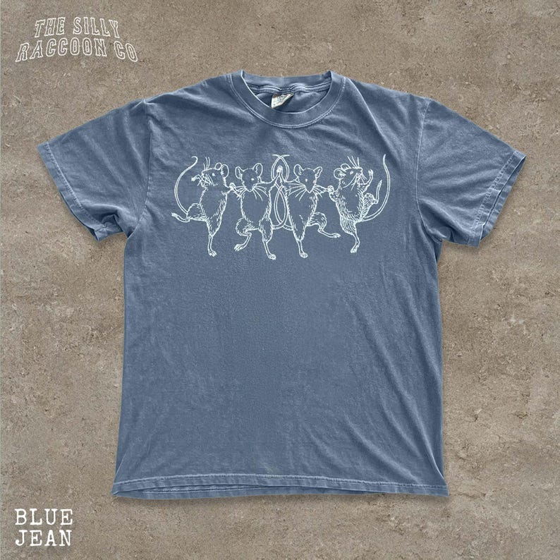A blue t-shirt with a white graphic design depicting a group of cats dancing together.