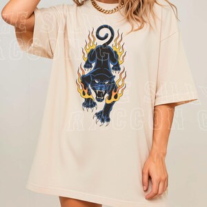 A woman wearing a white t-shirt with a graphic design of a black panther with flames on its back.