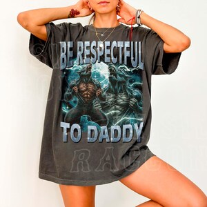 A person wearing a black t-shirt with a graphic design featuring two werewolves and the text "BE RESPECTFUL TO DADDY".