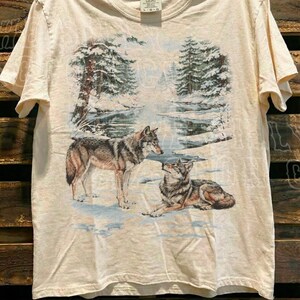 A t-shirt with a printed design depicting two wolves in a snowy forest setting.