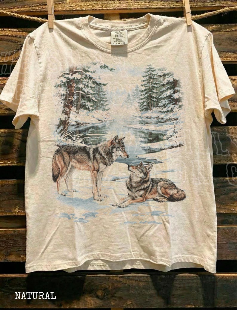 A t-shirt with a printed design depicting two wolves in a snowy forest setting.