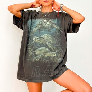 A woman wearing a black t-shirt with a graphic of three sea turtles swimming in the ocean.