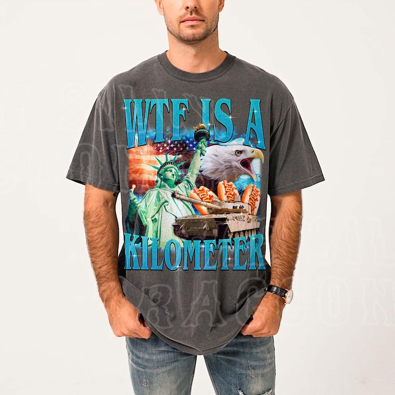 A man wearing a gray t-shirt with a graphic design featuring the Statue of Liberty, an eagle, and a sign that says "WTF IS A KILOMETER".