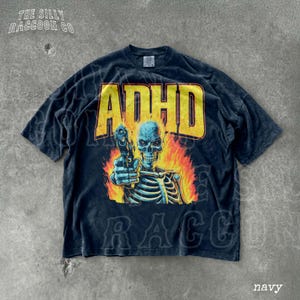 A navy blue t-shirt with a graphic design depicting a skeleton holding a gun and surrounded by flames.
