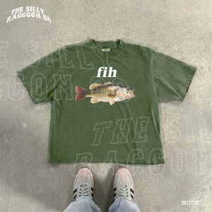 A pair of green t-shirts with a fish graphic and the word 'fih' printed on them, along with a pair of white sneakers.