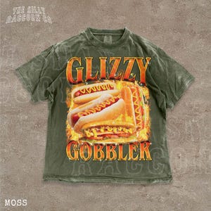 A t-shirt with a graphic design featuring two hot dogs on a bun, with flames around them, and the text "GLIZZY GOBBLER" prominently displayed.