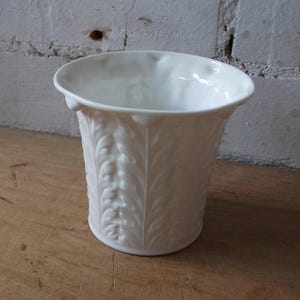May include: White ceramic vase with a fluted design. The vase has a wide mouth and a narrow base.