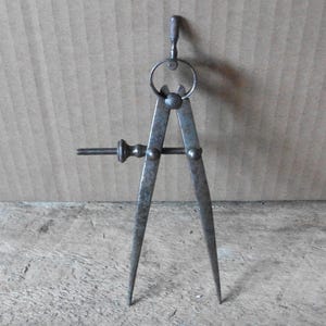May include: A vintage metal drafting compass featuring two pointed legs, a central threaded adjustment screw with a knurled knob, and a circular top handle with a textured grip. The tool has a weathered, dark gray patina throughout its surface.