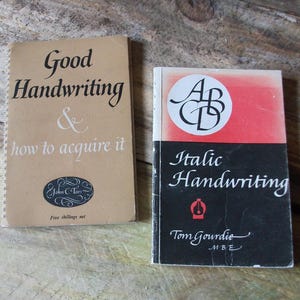 May include: Two vintage handwriting instruction books. One is titled "Good Handwriting & how to acquire it" with a spiral binding and a tan cover. The other is titled "Italic Handwriting" with a red and black cover.