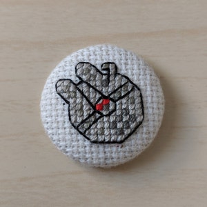 Puede incluir: Un botón de tela blanco con una imagen bordada en gris y negro de una Estrella de la Muerte de Star Wars.