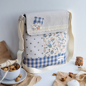 May include: A light gray fabric crossbody bag with a patchwork design featuring blue and white gingham, polka dots, and floral patterns. The bag has a white lace trim and a beige strap.