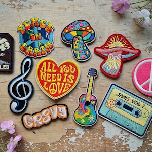 Può includere: Una collezione di toppe ricamate colorate a tema retrò. I disegni includono un fungo, un simbolo di pace, una chitarra, una chiave di violino, una cassetta e le parole "All You Need Is Love" e "Groovy".