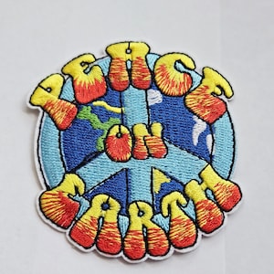 May include: Embroidered patch featuring the words "Peace on Earth" in yellow and red. The design includes a blue globe with green continents. The patch has a white border and is set against a white background.