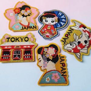 Puede incluir: Cinco parches bordados con temas japoneses: una persona en kimono con flores de cerezo, una figura pequeña con un paraguas azul con la etiqueta JAPAN, un templo rojo con la etiqueta TOKYO, un pez koi con la etiqueta JAPAN y una persona en kimono con la etiqueta JAPAN.