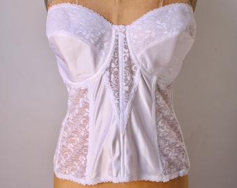 May include: A vintage white bustier with lace detailing. The strapless bodice features a central panel of lace, with lace accents on the sides and top. The bustier is displayed on a vintage dress form.