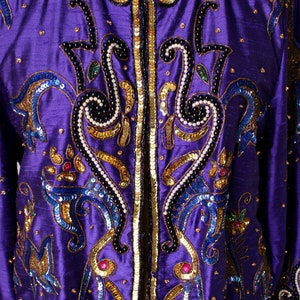 May include: A vibrant purple jacket with intricate embellishments. The jacket features gold sequins, blue and black beading, and decorative patterns. The design includes a round neckline and long sleeves. The jacket is a statement piece.