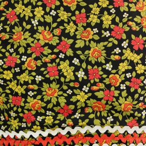 May include: Close-up of a floral fabric with a black background. The fabric features red, yellow, and white flowers with green leaves. The edges are trimmed with white and orange zigzag trim, creating a decorative border.