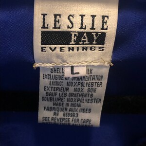 May include: A white tag with the text "LESLIE FAY EVENINGS" in black. The tag also includes fabric content details, size "L", and "MADE IN INDIA". The tag is against a blue fabric.