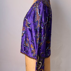 May include: A vintage purple jacket with intricate sequin and bead embellishments. The jacket features a detailed floral design in gold and blue, with a satin-like texture. The sleeves and collar are also adorned with the same decorative elements.