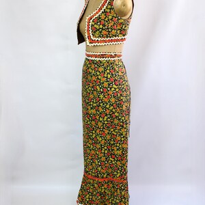 May include: A vintage two-piece outfit featuring a vest and a long skirt. The set is adorned with a floral pattern in red, yellow, and green on a black background. The edges are trimmed with white and orange lace.
