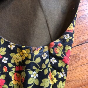 May include: Close-up of a black floral print fabric with yellow, orange, and white flowers and green leaves. The fabric has a dark background and a sheer, olive-green lining. The edges of the fabric are visible.
