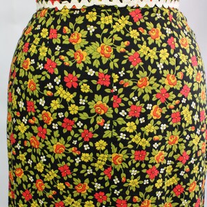 May include: A black skirt with a floral pattern featuring red, yellow, and green flowers. The waistband is trimmed with white and orange decorative trim. The skirt is a vintage style.