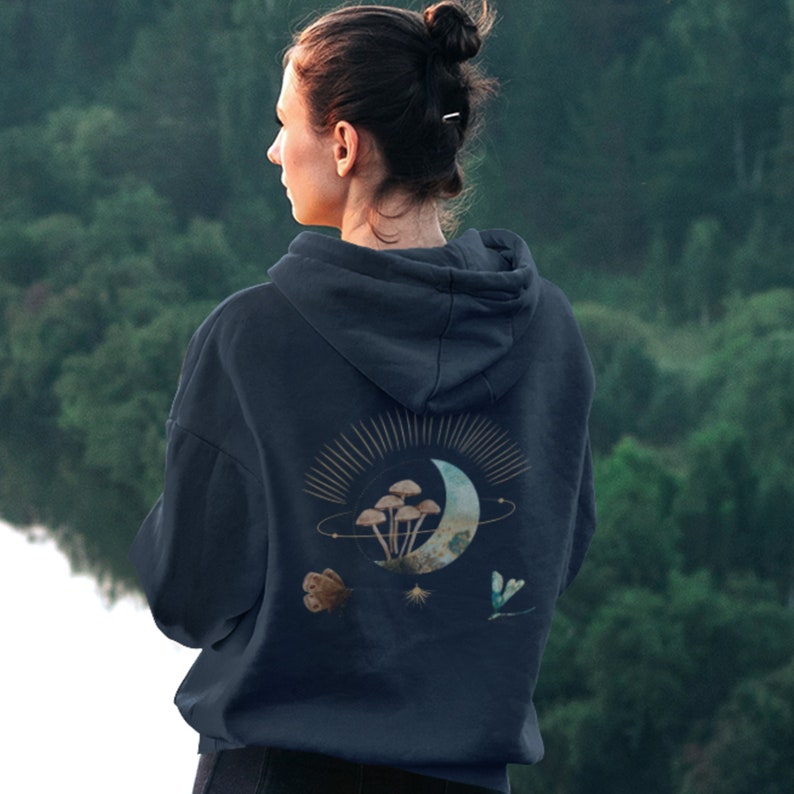 May include: Dark navy blue hoodie with a celestial design on the back. The design includes a crescent moon, mushrooms, stars, and a butterfly. The hoodie has a drawstring hood and a kangaroo pocket.
