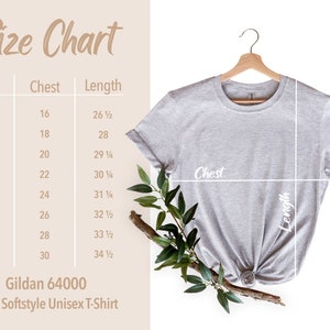 May include: A light grey Gildan 64000 Adult Softstyle Unisex T-Shirt hangs on a wooden hanger. A size chart shows chest and length measurements in inches for sizes XS to 4XL. Greenery accents the shirt.