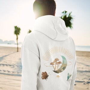 May include: White hoodie with a nature-themed design on the back. The graphic includes mushrooms, a crescent moon, a butterfly, and a dragonfly in watercolour tones. A casual, comfortable garment.