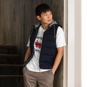 May include: A white t-shirt with the word "Party" printed three times, with a graphic of two red cups and a ping pong ball. The person is wearing a navy blue hooded vest and khaki pants.
