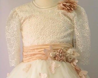 Puede incluir: Un vestido de tul blanco con un corpiño de encaje y una cinta de color melocotón. El vestido está decorado con flores y mariposas de color melocotón.