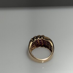 K&ouml;nnte beinhalten: Ein goldfarbener Ring mit mehreren Reihen kleiner, quadratisch geschliffener, roter Edelsteine. Der Ring hat ein breites Band und ein klassisches Design. Die Edelsteine sind eng aneinander gesetzt und bilden eine durchgehende, lebendige Oberfl&auml;che.