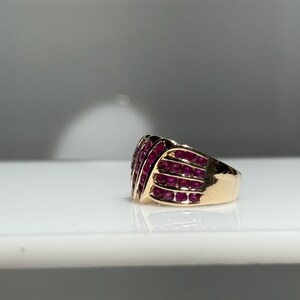 K&ouml;nnte beinhalten: Ein goldener Ring mit einer Ansammlung kleiner, runder, rubinroter Steine. Die Steine sind in Reihen angeordnet und bilden eine strukturierte Oberfl&auml;che. Der Ring hat einen dicken Schaft und ein poliertes Finish.