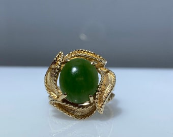 Könnte beinhalten: Ein goldener Ring mit einem grünen Jade-Stein, der in einem wirbelnden Design gefasst ist.