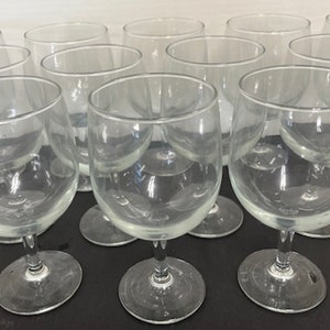 May include: A set of ten clear glass wine glasses with a round bowl and a stem. The glasses are arranged in a semi-circle on a black surface.