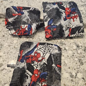 May include: Three Spider-Man themed pouches. The pouches feature a repeating pattern of Spider-Man in action poses, along with spiderwebs and cityscapes. The color scheme is primarily red, blue, black, and white.