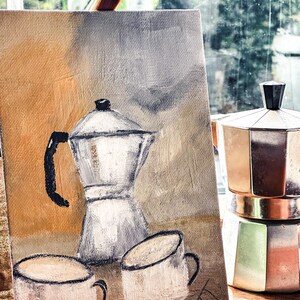 May include: An oil painting on canvas shows a coffee pot and two mugs in neutral tones. A metal stovetop espresso maker sits beside the painting. A paintbrush rests on top of the canvas.
