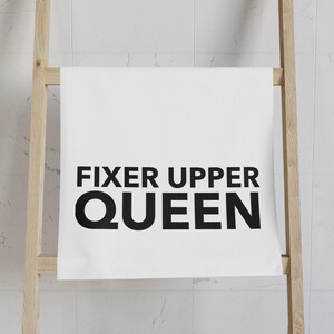 May include: White kitchen towel with black text that reads "Fixer Upper Queen".