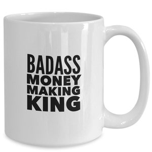 May include: White ceramic coffee mug with black text that reads "BADASS MONEY MAKING KING".